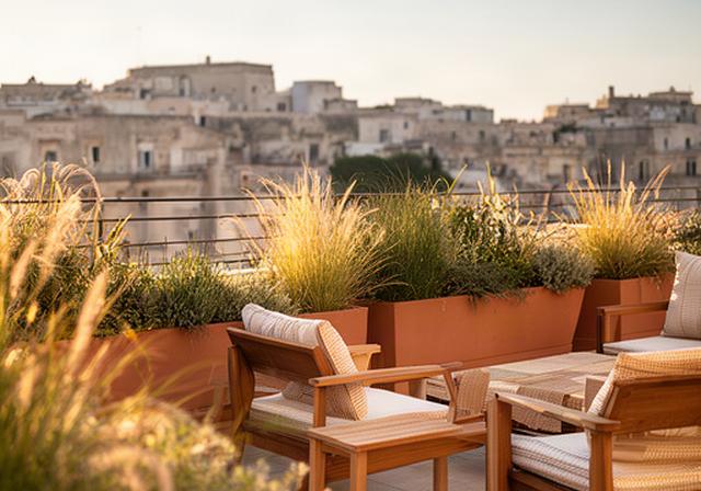 Terrazza urbana a Modica trasformata in zona relax con vasi, graminacee e sedute in legno