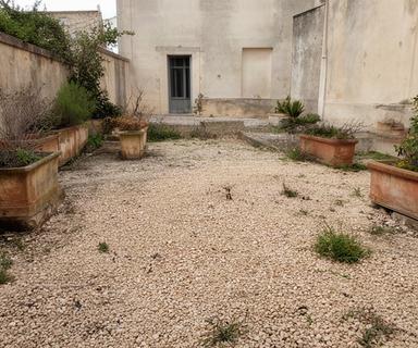 Corte di una piccola struttura ricettiva prima della pulizia, con vecchie fioriere e ghiaia irregolare